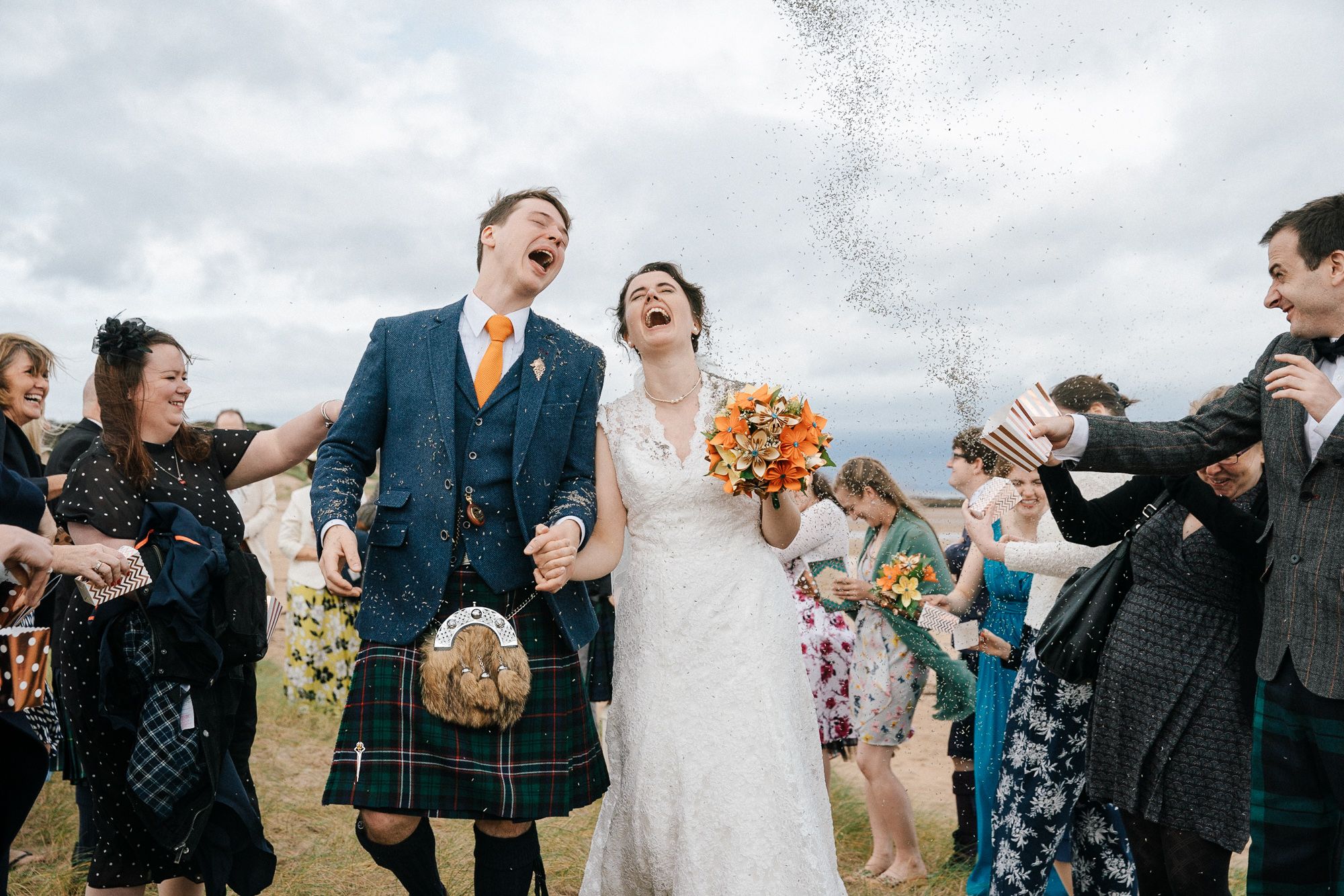 bride and groom laughing while wedding guests throw confetti